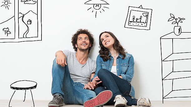 Portrait Of Happy Young Couple Sitting On Floor Looking Up While Dreaming Their New Home And Furnishing